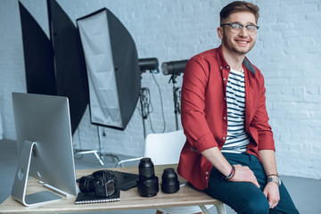Fototapete - Smiling photographer sitting on table with camera and computer