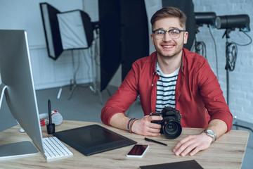 Fototapete - Happy freelancer man sitting by working table with camera and graphic tablet