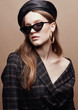 Fashion portrait of beautiful young woman in black leather beret cap, plaid jacket and cat eye retro sunglasses with massive golden earrings