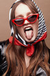 © monchak - Retro style portrait of amazing young woman in red cat eye sunglasses and retro headscarf with black, white and red stripes. Girl shows tongue.