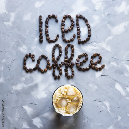 Fotografie, Obraz A glass of iced coffee with milk next to the inscription "ice coffee" from coffee beans on a gray concrete background