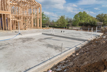Slab-on-grade foundation footing timber frame house under construction in Irving, Texas, USA. Shallow raft structural engineering transfers building loads to earth very near to surface, pile of earth