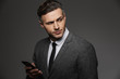 © Drobot Dean - Image of young unshaved man dressed in business costume chatting or working on mobile phone and looking aside, isolated over gray background