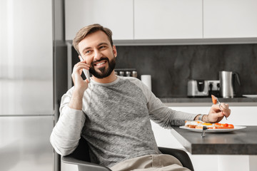 Sticker - Handsome bachelor 30s with beard having mobile conversation, while eating healthy food at dinner in flat