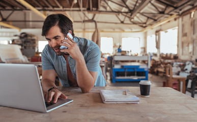 Smiling woodworker discussing designs over a cellphone and working online