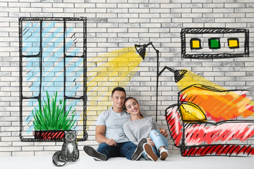 Happy young couple sitting on floor near brick wall in their new apartment. Moving house concept