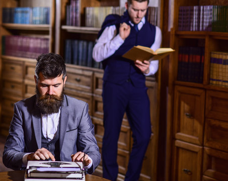 Man with beard typing on typewriter while his friend reading