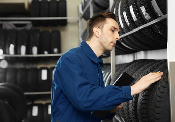 Poster - Young male mechanic with clipboard near tires in automobile service center