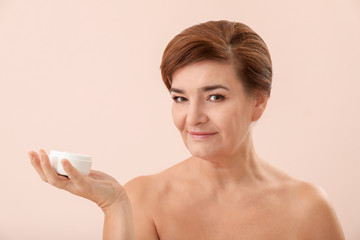 Wall Mural - Portrait of beautiful mature woman with jar of anti-aging cream on light color background. Skin care concept