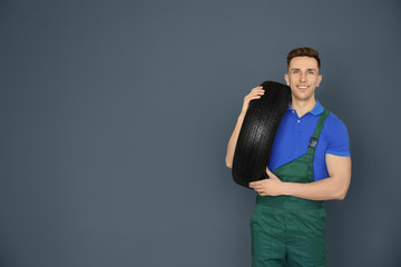 Poster - Male mechanic with car tire on grey background