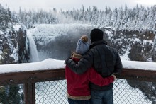 Couple In Warm Clothing Looking At Waterfall
