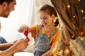 Wall Mural - family, hygge and people concept - happy father and little daughter playing tea party in kids tent at night at home