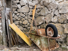 Old Rusty Wheelbarrow Lying On The Floor In Front Of Stone Wall