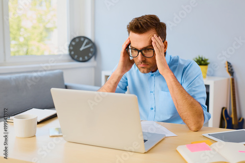 Fotografia Worried man working from home office looking on laptop
