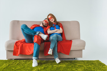 Wall Mural - tired couple in superhero costumes sleeping while sitting on sofa on grey