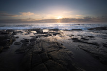 Landscape Image Of Waves Breaking Against The Rocks At Low Tide During Sunrise Along The North Coast Of South Africa. The Sun Rises Behind Low Clouds.