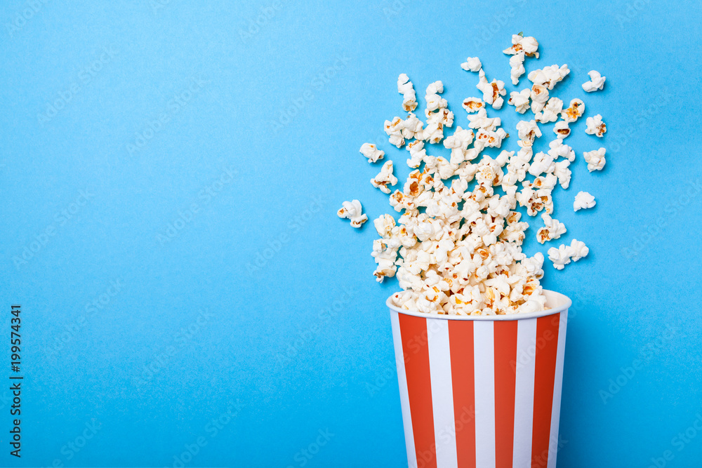 Spilled popcorn and paper bucket in red strip on blue background. Copy space for text - obrazy, fototapety, plakaty 