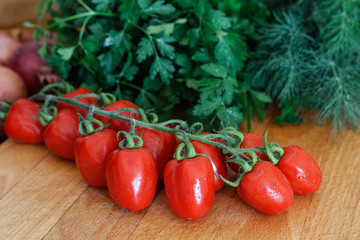 Wall Mural - Grape tomatoes on vine  on wood chopping board in front of a bunch of fresh dill and parsley.