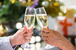cheerfuls Friends toasting sparkling wine. Close-ups hands of two friends toasting wine glass in the dinner party for celebrating new year on the bokeh of light decorate on christmas tree background.