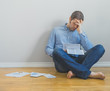 Sad man sitting at the floor and looking at his bills.