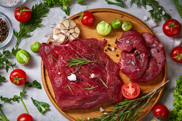 Wall Mural - Still life of raw beef meat with vegetables on wooden plate over white background, top view, selective focus