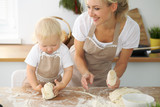 Fototapeta  - Little girl and her blonde mom in red aprons  playing and laughing while kneading the dough in the kitchen. Homemade pastry for bread, pizza or bake cookies