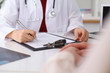 © rogerphoto - Close up of a female doctor filling up  an application form while consulting patient