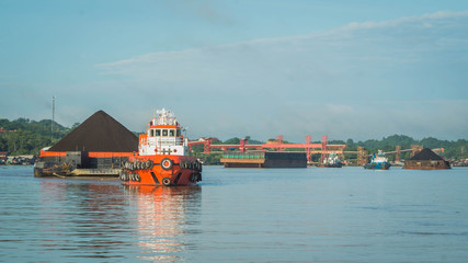 tugboats pull heavy load barge of black coal in Mahakam river, Borneo, Indonesia