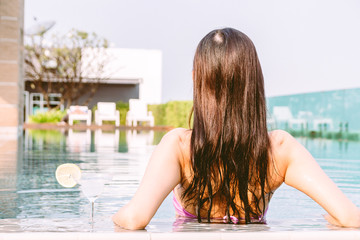 Woman wearing two piece bikini in swimming pool on summer vacation relaxing at resort spa