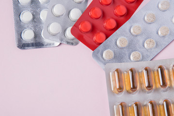 Different tablets and pills in the package and without it on a pink background