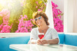 Attractive mature woman sits in a blooming garden with a glass of wine, summer vacation