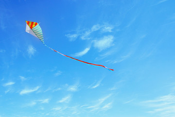 Wall Mural - Colorful kite flying in the blue sky through the clouds.