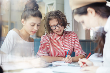 Three college girls making notes about their ideas while working over creative project for one of college subjects