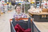 Fototapeta  - sale, consumerism and people concept - happy little girl with food in shopping cart at grocery store