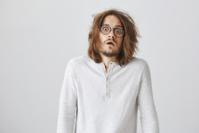 Hair Stand From Shock. Portrait Of Good-looking European Male Model In Trendy Glasses With Messy Haircut Tilting Backwards From Shock And Amazement, Dropping Jaw Over Gray Background