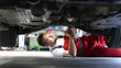 © industrieblick - Automechaniker repariert Fahrzeug in einer Werkstatt in Arbeitskleidung am Unterboden - Closeup // Car mechanic repairs vehicle in a workshop in work clothes on the underbody