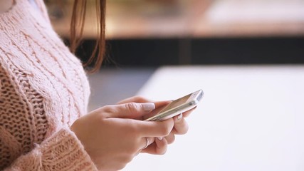 Wall Mural - Closeup of young woman`s hands browsing the net using a smartphone in a spacious shopping mall. The hands are well-groomed with stylish manicure