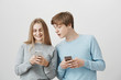 © Cookie Studio - Two positive friends editing selfie to post it in social network. Friendly loving couple, girlfriend showing boyfriend cute video in internet, holding smartphone while guy peeking at screen curiously