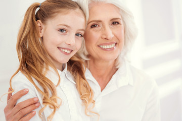 Wall Mural - She is my everything. Selective focus on an adorable preteen girl with ponytails looking into the camera with a cheerful smile on her face while sitting on the lap of her loving granny