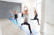 © uv_group - Group of people doing yoga warrior pose at white studio with gesture of will. Fitness class, sport and healthy lifestyle concept