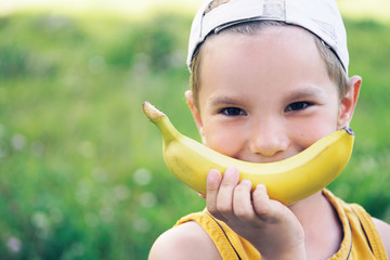 Face of a beautiful young caucasian boy in cap with banana smile on nature background.