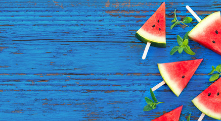 Summer background. Watermelon fruit slice popsicles on a  blue wood background with mint leaves, flat lay.