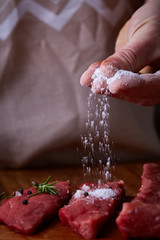 Sticker - Strong professional man's hands spilling salt on raw beefsteak, selective focus, close-up