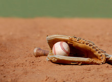 An Old Baseball Glove Cradling A Worn Ball Lays In The Dusty Clay Of The Infield At A Ball Park On A Sunny Day. Shallow Depth Of Field. Copy Space.