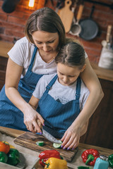 Poster - Adult woman teaching little girl to cut the cucumber on table on kitchen.