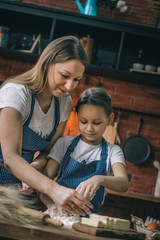 Poster - Cheerful woman with daughter making dough on kitchen at home. 