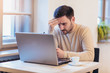 © Mediteraneo - Man stressed while working on laptop. Upset disappointed young businessman sitting at workplace with hands on head.