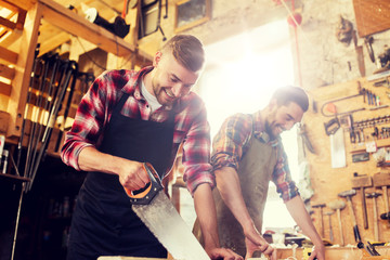 Wall Mural - profession, carpentry, woodwork and people concept - carpenters working with saw and wood plank at workshop