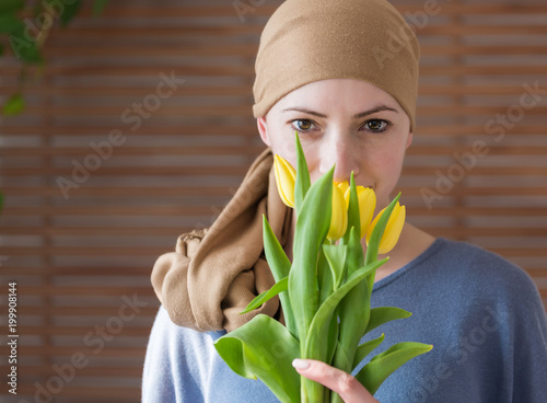 Fotografía Young positive adult female cancer patient holding bouquet of yellow tulips, smiling and looking at camera