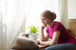 © andreaobzerova - Young positive adult female cancer patient sitting in the kitchen by a window with her pet cat, smiling.